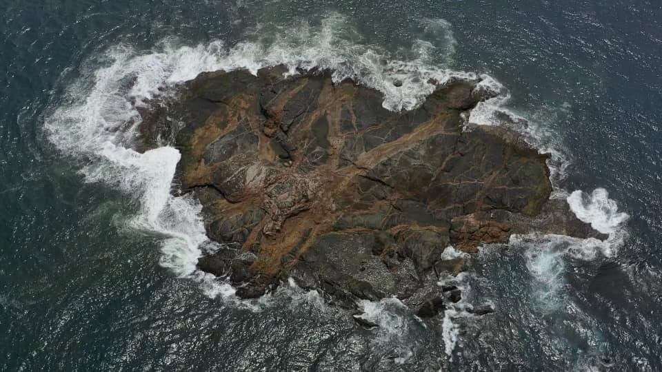 Aerial view of waves breaking around a lone rock island